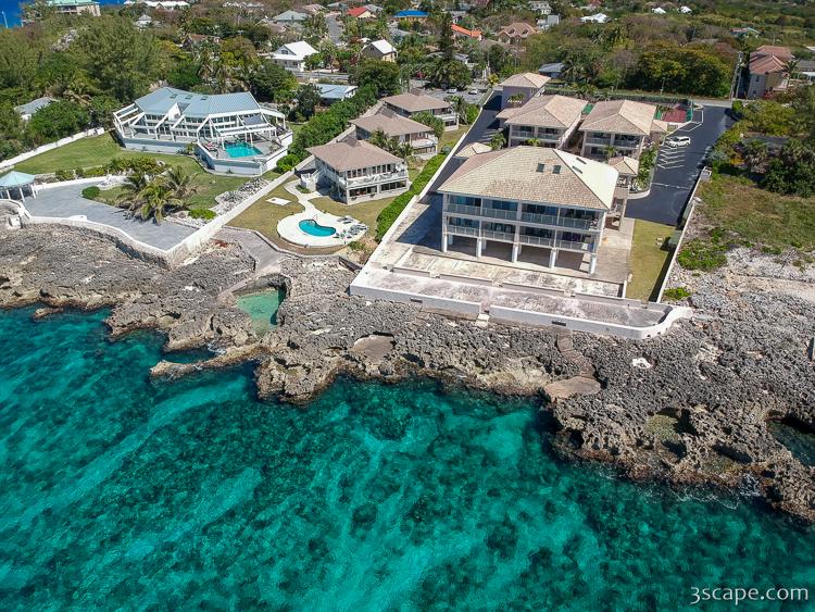Aerial view of an oceanfront condo complex on Grand Cayman's rocky West Bay coastline, with a pool and turquoise water below