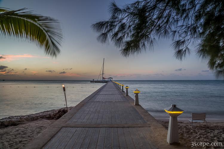 Rum Point pier at dusk, lit by tiki torches with a sailboat moored at the end