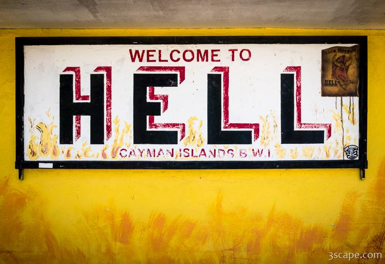 A yellow wall with a black and red sign reading Welcome to Hell, Cayman Islands, marking the ironshore rock formation in West Bay